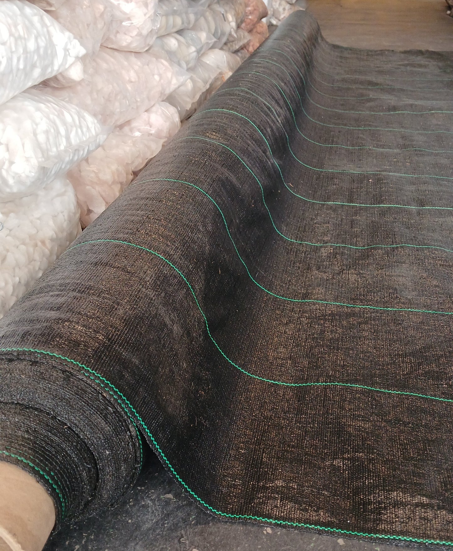 Roll of black weed barrier fabric with green edges on a construction site.