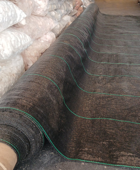 Roll of black weed barrier fabric with green edges on a construction site.