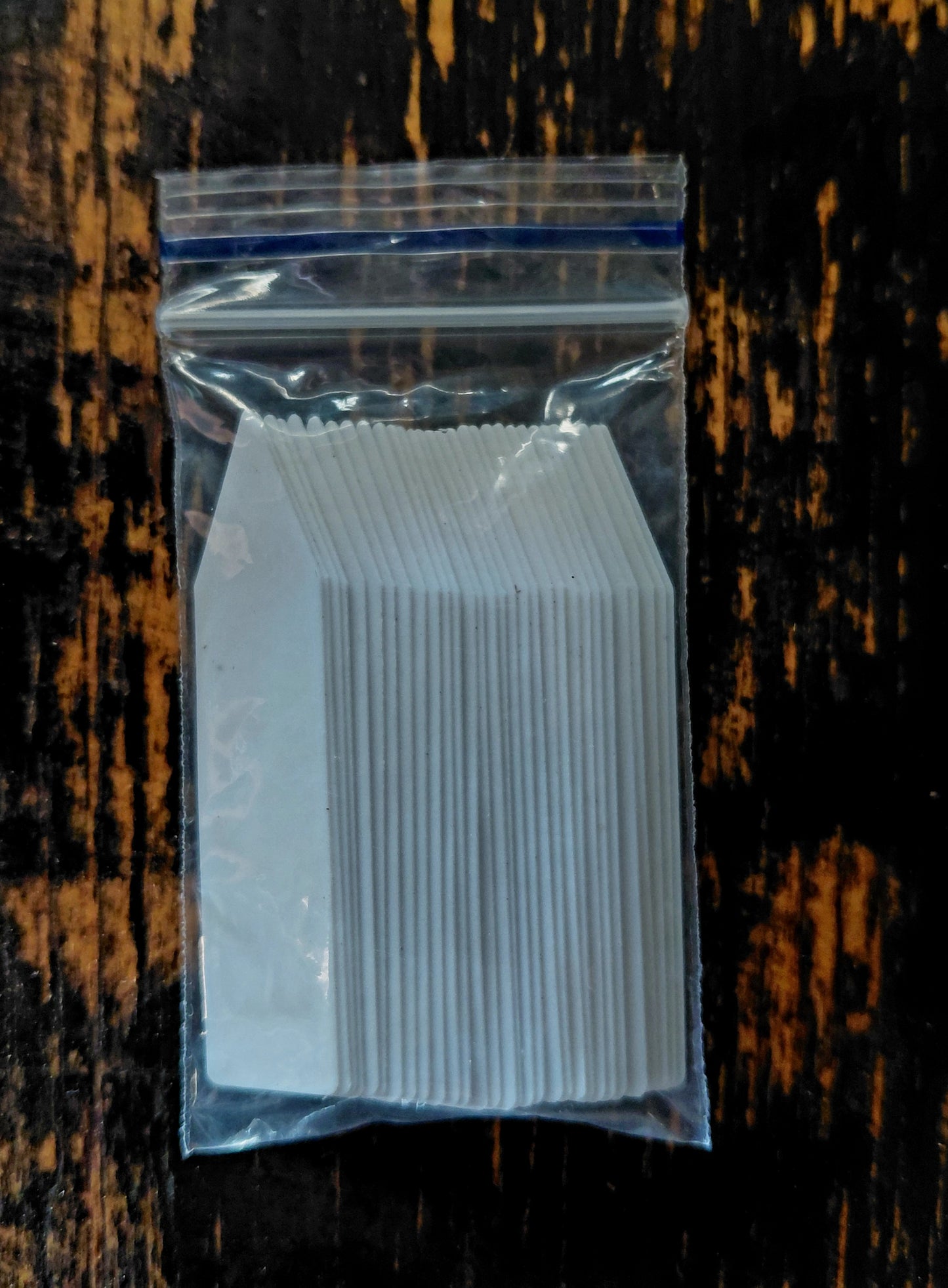 Clear plastic bag filled with white rectangular plant tags on a wooden surface